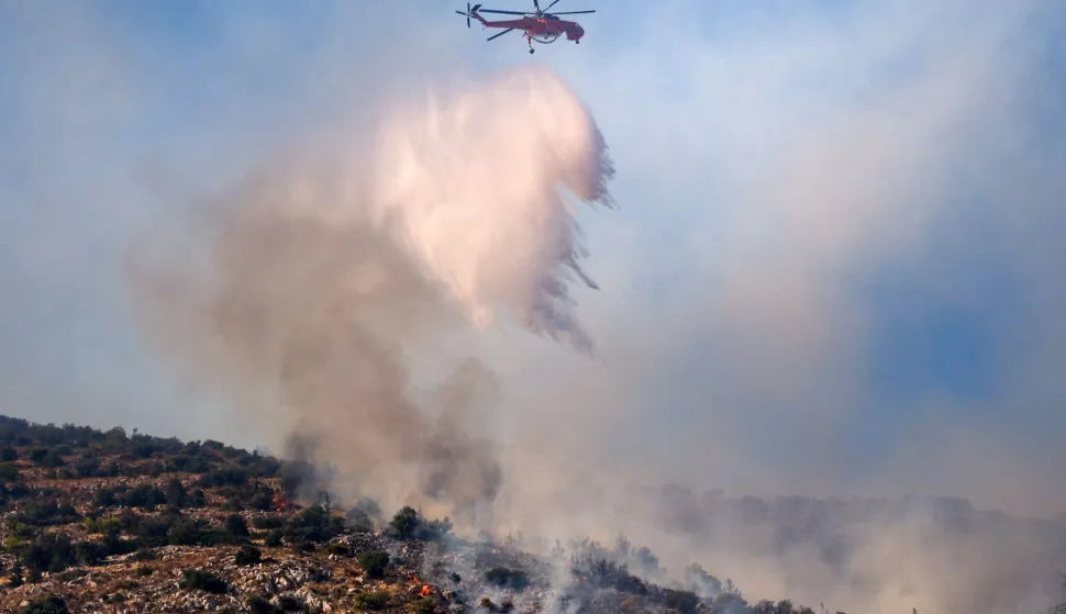 A firefighting helicopter drops water on a wildfire in Haidari, a suburb west of Athens, on July 31, 2026. New wildfires fed by strong winds broke out in Greece on July 31, 2026 giving firefighters little respite and forcing Civil Protection officials to order the partial evacuation of part of a suburb west of Athens. (Photo by Aris Oikonomou/AFP)