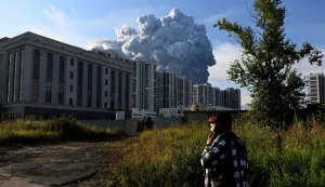 A person speaks on a mobile phone as smoke rises above residential buildings from a warehouse for a Russian e-commerce giant near Saint Petersburg after being hit by Ukrainian drones early on July 24, 2026 morning, triggering a fire that sent smoke pouring over the historic city, according to local officials. Kyiv has targeted Saint Petersburg as it steps up long-range drone strikes on Russian energy, military and logistics sites in recent weeks. Russia's defence ministry said its forces shot down some 571 drones overnight over more than a dozen regions and Crimea, the Black Sea peninsula that Russia annexed in 2014. (Photo by AFP)