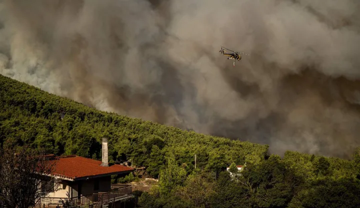 A firefighting helicopter flies as smoke rises from a wildfire in the area of Porto Germeno, some 70 kilometres (45 miles) northwest of Athens in the region of Viotia, on August 2, 2026. Hundreds of firefighters in Greece battle to save a popular coastal resort northwest of Athens as violent winds continued to lash the country, hampering operations. Hit hard by the climate crisis like the rest of the Mediterranean region, the country is plagued by wildfires every summer due to high temperatures, frequent heatwaves, and drought. (Photo by Angelos TZORTZINIS/AFP)