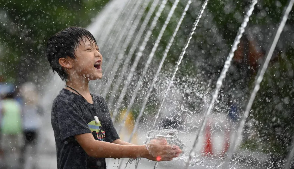 A child cools off in a fountain in Seoul on August 4, 2026. South Korea's summer heat has killed 16 people so far this year, the interior ministry said August 4, as the nation swelters in a wave of searing weather. (Photo by GREG BAKER/AFP)