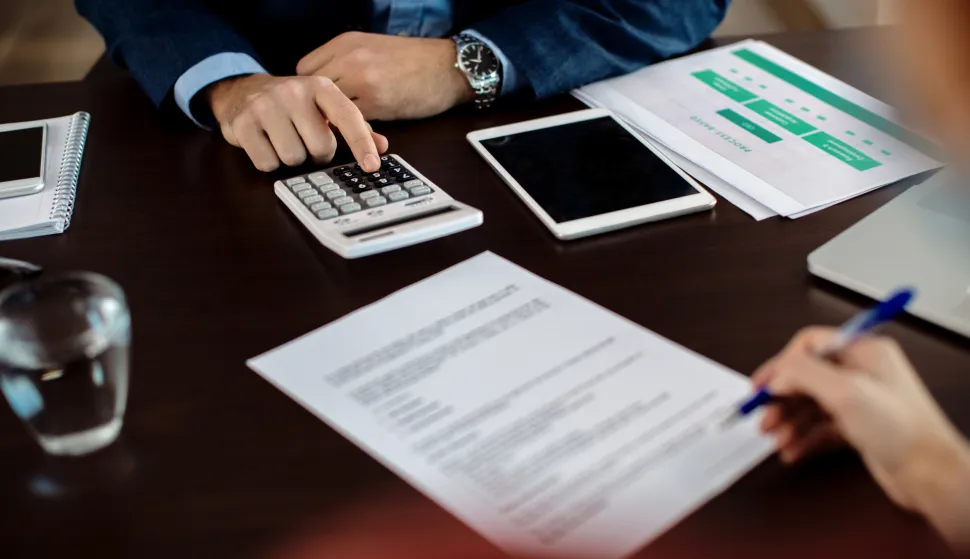 Close-up of insurance agent calculating costs an agreement while having a meeting with a client.Građani su nenamjenske kredite podizali uz stambene, &raquo;krpali&laquo; su njima kućni budžet, ali i kretali u investicije, banka kredit dug novac ilustracija magnific