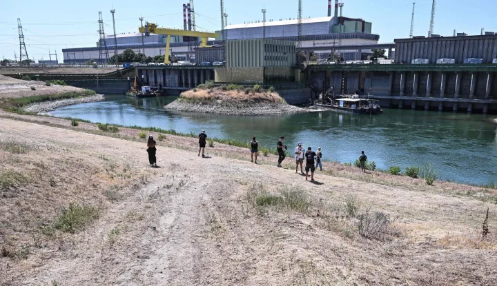 Journalists stand in front of Paks Nuclear Power Plant?s water intake structure and cold-water canal working with water from the river Danube in Paks on July 31, 2026. Amid prolonged heatwave conditions and air temperatures exceeding 35?C, the Danube has fallen to record low levels, creating a critical operational challenge for the plant. The extraordinary low-water situation has raised the prospect of a complete shutdown to ensure the continued safe cooling of the reactor units. (Photo by Attila KISBENEDEK/AFP)