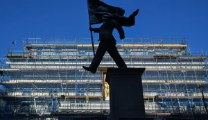 A statue which suddenly appeared the day before, bearing the signature of British street artist Banksy etched onto its base, is pictured in Waterloo Place in central London early morning on April 30, 2026. A large statue has appeared on a plinth in central London with Banksy's name scrawled on the base, prompting speculation on April 30, 2026 that it may be the British street artist's latest work. The statue -- of a suited man marching, with one leg off the plinth, while carrying a flag that is covering his face -- reportedly first emerged just off Pall Mall on Wednesday. (Photo by Richard A. Brooks/AFP)/RESTRICTED TO EDITORIAL USE - MANDATORY MENTION OF THE ARTIST UPON PUBLICATION - TO ILLUSTRATE THE EVENT AS SPECIFIED IN THE CAPTION