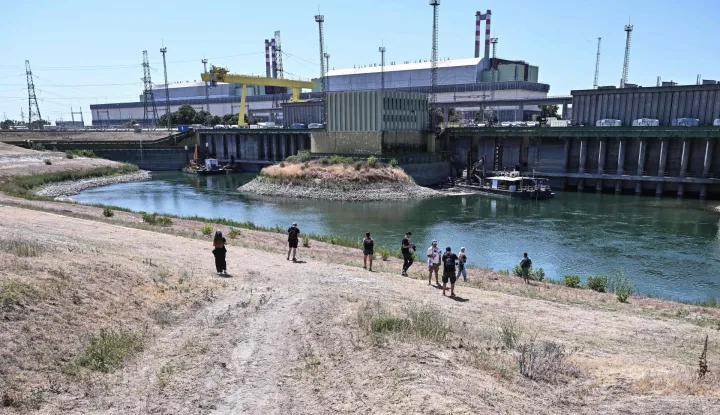 Journalists stand in front of Paks Nuclear Power Plant?s water intake structure and cold-water canal working with water from the river Danube in Paks on July 31, 2026. Amid prolonged heatwave conditions and air temperatures exceeding 35?C, the Danube has fallen to record low levels, creating a critical operational challenge for the plant. The extraordinary low-water situation has raised the prospect of a complete shutdown to ensure the continued safe cooling of the reactor units. (Photo by Attila KISBENEDEK/AFP)