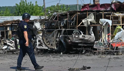 EDITORS NOTE: Graphic content/A Ukrainian law enforcement officer walks past a burnt-out car next to a destroyed building following an air attack in Pechenigy, Kharkiv region on August 18, 2026, amid the Russian invasion of Ukraine. A Russian attack on a village in the Kharkiv region of northeast Ukraine killed 10 people, Kyiv said on August 18, 2026, vowing to respond. (Photo by SERGEY BOBOK/AFP)
