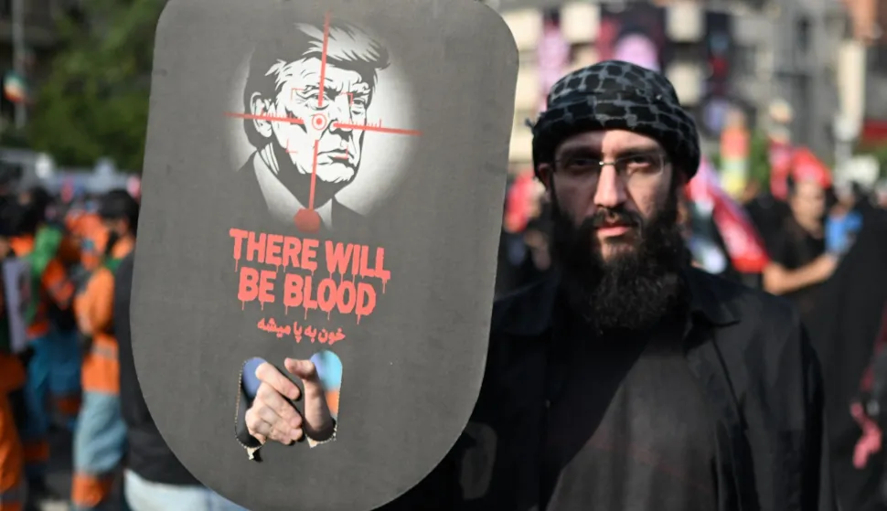 A man holds a placard depicting US President Donald Trump and displaying the words "There Will Be Blood" as they gather at Ferdowsi Square for the funeral procession of Iran's slain Supreme Leader Ali Khamenei in Tehran July 6, 2026. Massive crowds are expected on July 6 for the funeral procession of late Iranian supreme leader Ali Khamenei in Tehran, with authorities hoping to avoid a repeat of the chaos that accompanied his predecessor's funeral. (Photo by Wakil Kohsar/AFP)/