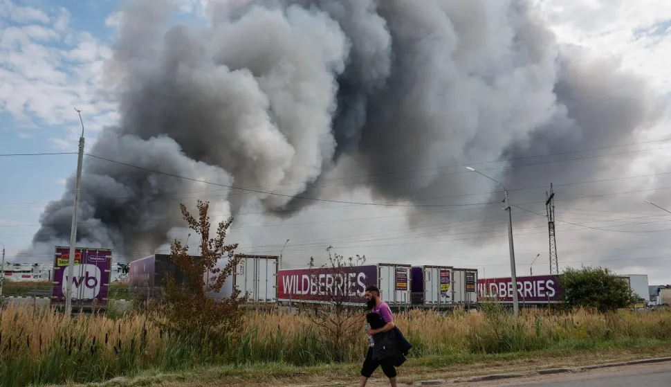 A Wildberries emloyee walks past a plume of smoke rises during a fire at Russian e-commerce firm Wildberries' logistics complex near the town of Podolsk, outside Moscow on August 16, 2026. Hundreds of drones targeted Moscow on August 16, 2026 as Russia launched missile strikes that killed three people and wounded more than a dozen in Kyiv and other Ukrainian cities, officials on the two sides said. Ukraine has increasingly targeted warehouses linked to the Wildberries online retailer, arguing its strikes are a response to Moscow's bombardment of Ukrainian towns and infrastructure. (Photo by TATYANA MAKEYEVA/AFP)