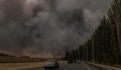 Cars drive on a road as smoke rises in the distance from a warehouse following a Russian air attack near Boryspil, Kyiv region on August 27, 2026, amid the Russian invasion of Ukraine. (Photo by Roman PILIPEY/AFP)
