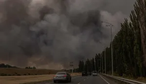 Cars drive on a road as smoke rises in the distance from a warehouse following a Russian air attack near Boryspil, Kyiv region on August 27, 2026, amid the Russian invasion of Ukraine. (Photo by Roman PILIPEY/AFP)