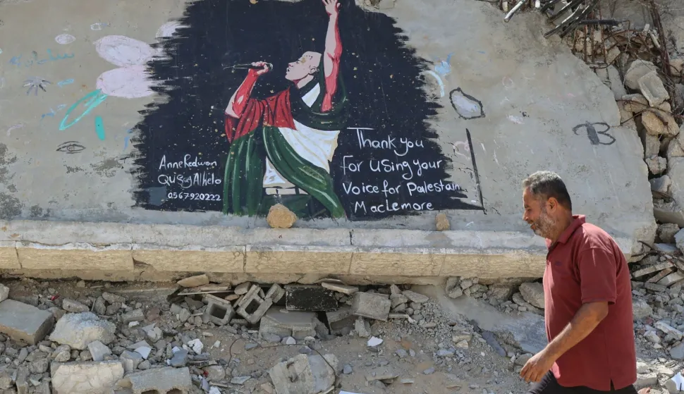 A Palestinian man walks past a mural painted on the rubble of a destroyed building and dedicated to US rapper, singer, dancer and DJ, Benjamin Haggerty, known as Macklemore, in Gaza City on September 19, 2026. Macklemore was booted from Ed Sheeran's US tour after provoking outrage by saying "free Palestine" at one of the stadium stops this month, the US rapper said on September 14. The artist made headlines after telling the crowd at MetLife Stadium in New Jersey that he wanted the people of Gaza and the West Bank to know they had not been forgotten. (Photo by Omar AL-QATTAA/AFP)