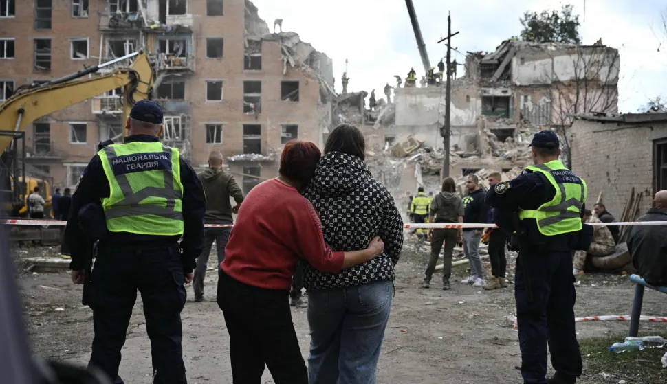 TOPSHOT - Local residents hug as they look at a multi-floor residential building destroyed following a Russian aerial strike in Pryluky on October 7, 2026, amid the Russian invasion of Ukraine. In Pryluky, the death toll has risen to nine people, including three children, and 40 people are known to have been injured, including seven children, the Emergency Service said on October 7, 2026. (Photo by Genya Savilov/AFP)