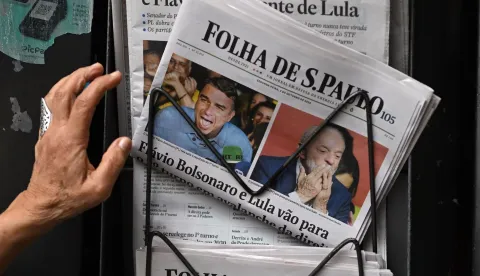 A person reaches for copies of the newspaper Folha de Sao Paulo displaying coverage of Brazil's presidential election results at a newsstand in Sao Paulo, Brazil, on October 5, 2026. The Sao Paulo stock exchange opened sharply higher on October 5 after a surprise first round election result saw right-wing senator Flavio Bolsonaro edge past incumbent Luiz Inacio Lula da Silva. (Photo by Luis ROBAYO/AFP)