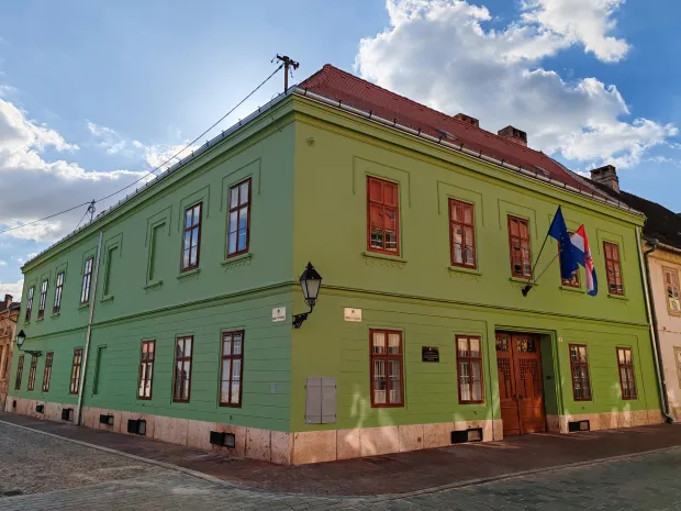 O jednokatnici sagrađenoj na jugozapadnom uglu Ulice Franje Kuhača i Ulice dr. Danice Pinterović već smo pisali u ovoj kolumni, a razlog za objavu jo&scaron; jednog teksta je upravo dovr&scaron;ena obnova njezina pročelja.listopad 2026.