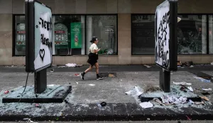 TOPSHOT - A pedestrian runs past damages and a broken frontage windows of a shop a day after riot and looting following a nationwide protest against the "high cost of living", in Lyon central-eastern France on October 18, 2026. France's Prime Minister said 1,200 people were arrested in protests across the country on October 17, and 150 police were hurt during clashes between police and protesters. Massive looting and multiple blazes gripped France as nationwide marches against soaring inflation degenerated into street violence of "extreme intensity". (Photo by JEFF PACHOUD/AFP)