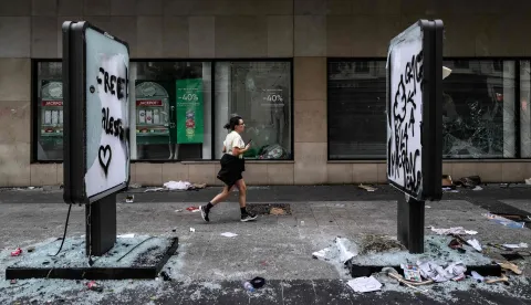 TOPSHOT - A pedestrian runs past damages and a broken frontage windows of a shop a day after riot and looting following a nationwide protest against the "high cost of living", in Lyon central-eastern France on October 18, 2026. France's Prime Minister said 1,200 people were arrested in protests across the country on October 17, and 150 police were hurt during clashes between police and protesters. Massive looting and multiple blazes gripped France as nationwide marches against soaring inflation degenerated into street violence of "extreme intensity". (Photo by JEFF PACHOUD/AFP)