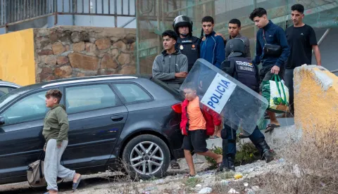 Migrants, including at least two minors, carry their belongings as Spanish police round up migrants sleeping rough outside the Tarajal warehouses on the outskirts of Spain's north African enclave of Ceuta on October 18, 2026. Scores of migrants remain sleeping rough in outlying neighborhoods of the city since the massive influx of tens of thousands of migrants from Morocco in late July, fueling tension in this Spanish North African enclave of some 80,000 inhabitants. Migrants are being transported by bus to police facilities, with minors taken to the National Police headquarters and adults transferred to the Tarajal Temporary Assistance Centre for Foreigners (CATE) for identification, registration and screening. (Photo by Antonio Sempere/AFP)