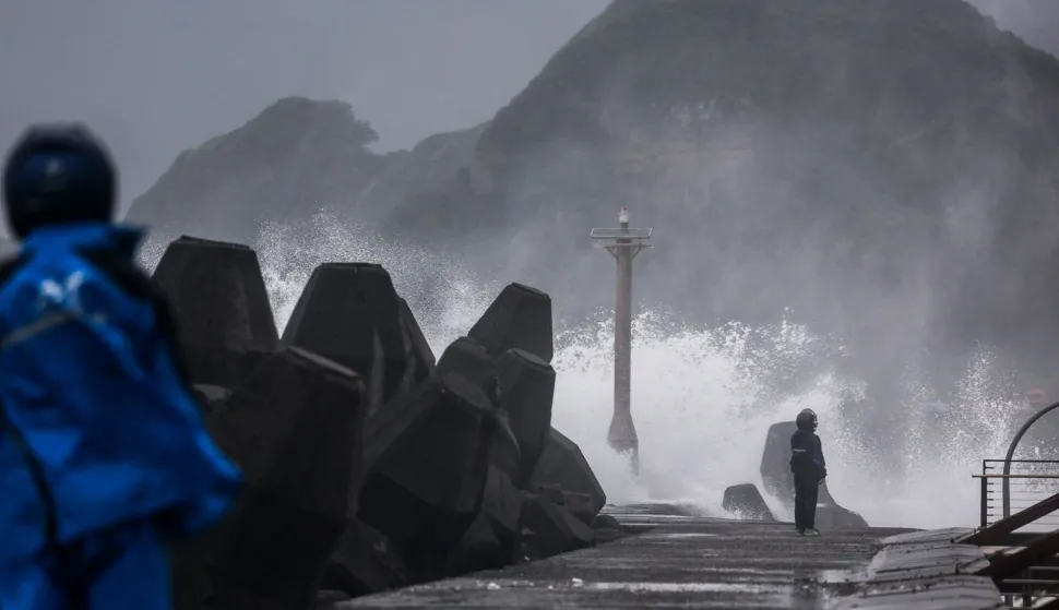 People stand on a breakwater as waves crash against it as Typhoon Champi approaches Taiwan, in Keelung on October 23, 2026. (Photo by I-Hwa Cheng/AFP)