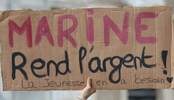 A protester holds a placard reading "Marine give back the money, the youth needs it" during a demonstration "against racism, fascism and imperialism" on the sidelines of the Congress of the Far-right party Rassemblement National (RN) in Orleans, central France on October 24, 2026. Amid another Saturday of protests under tight security across France, Orleans is hosting the National congress of the Far-right party Rassemblement National and preparing for a record-breaking demonstration, on the eve of their first major campaign rally. (Photo by ROMAIN PERROCHEAU/AFP)