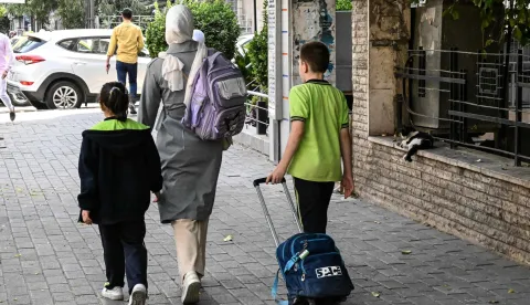 Children return home after a day at school in Damascus on October 26, 2026. Changes to Syria's official school textbooks including to remove or edit images of women and artwork have sparked criticism and revived fears of an Islamisation of society under the new authorities. (Photo by LOUAI BESHARA/AFP)